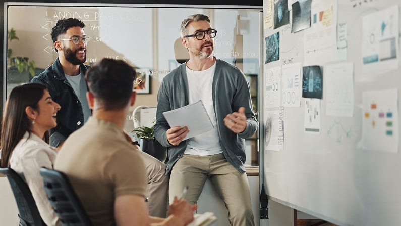 Illustratie van het profiel van de "participatieve manager". De manager en zijn team zitten voor het whiteboard om samen ideeën uit te wisselen.