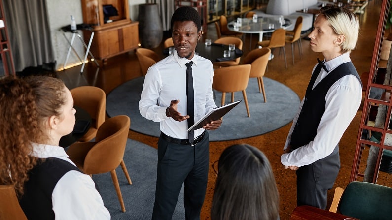 In a top-of-the-range restaurant, the manager holds a team meeting with the waiters.